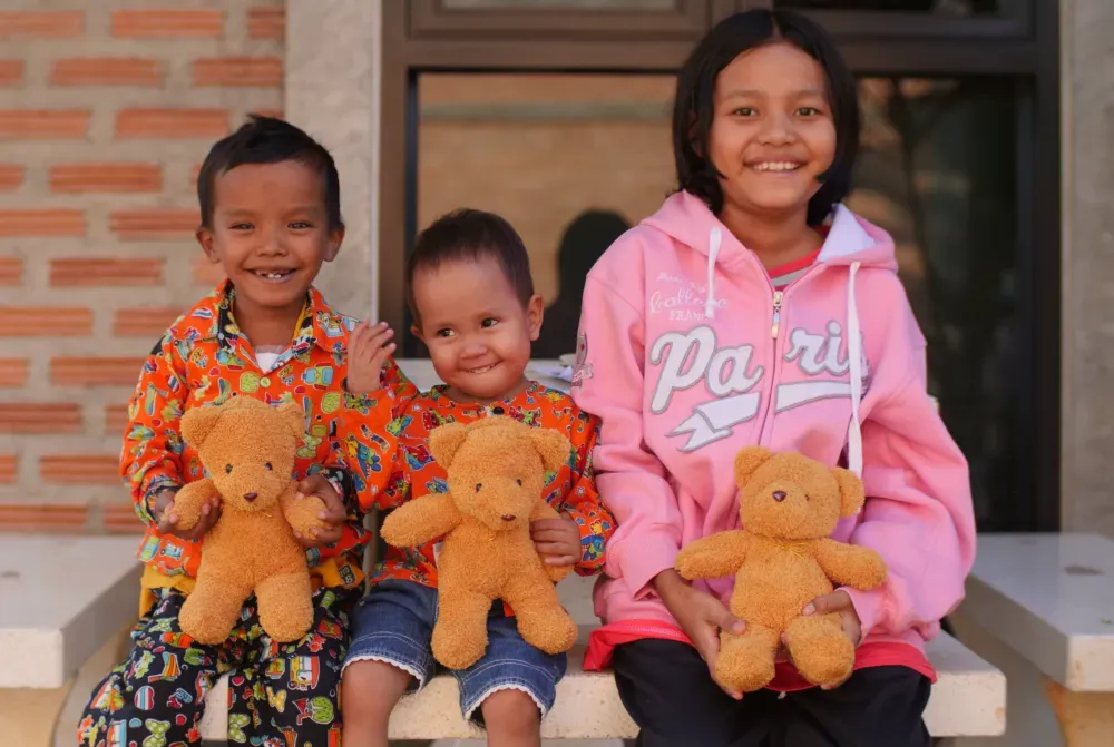 Three young patients supported by the Referral Services Program sit together with their teddy bears before departure.